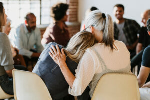 Woman leaning on another woman's shoulder during group therapy session.