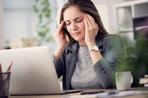 Woman gently presses fingers on temples while sitting at a desk in an office.