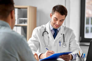 A pain specialist in a white coat takes notes on a clipboard during a patient consultation in a medical office.
