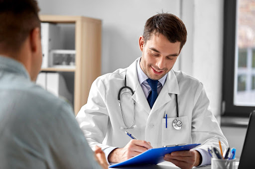 A pain specialist in a white coat takes notes on a clipboard during a patient consultation in a medical office.